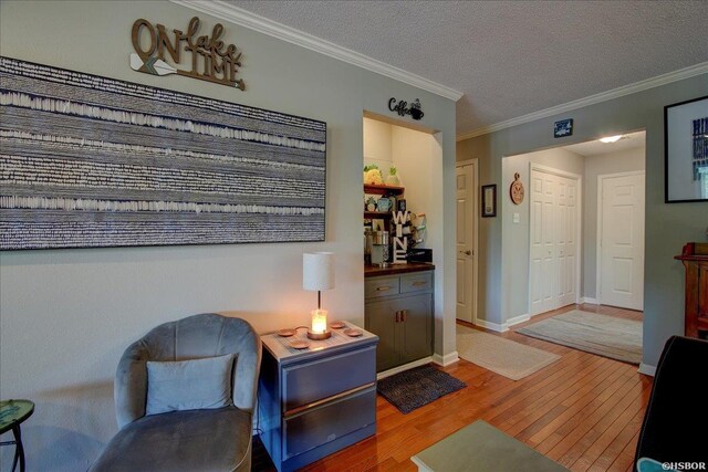 sitting room with crown molding, a textured ceiling, baseboards, and wood finished floors