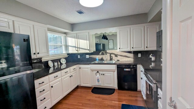 kitchen with a sink, visible vents, light wood-style floors, white cabinets, and black appliances