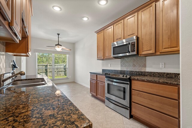 kitchen with stainless steel appliances, a sink, tasteful backsplash, brown cabinetry, and dark stone countertops