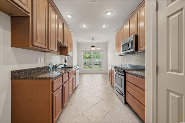 kitchen featuring light tile patterned floors, stainless steel appliances, a sink, brown cabinets, and dark stone counters