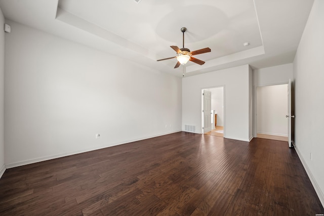 unfurnished bedroom with a tray ceiling, dark wood finished floors, visible vents, ceiling fan, and baseboards