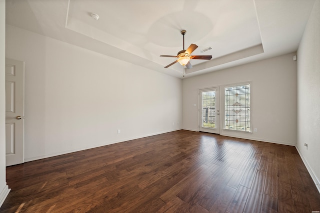 unfurnished room with ceiling fan, dark wood-style flooring, visible vents, baseboards, and a tray ceiling