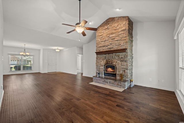 unfurnished living room with lofted ceiling, ceiling fan with notable chandelier, dark wood finished floors, and a stone fireplace