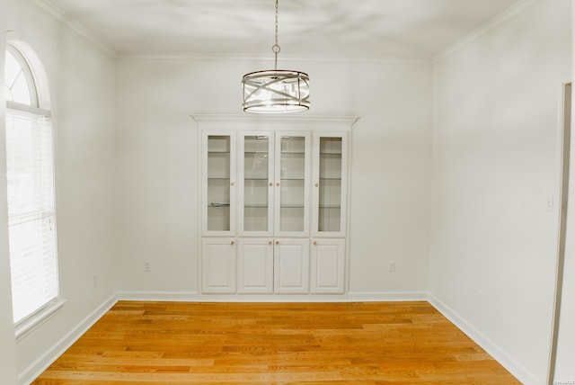 unfurnished dining area with ornamental molding, light wood-type flooring, a notable chandelier, and baseboards