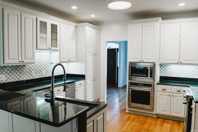 kitchen with light wood finished floors, decorative backsplash, glass insert cabinets, stainless steel appliances, and white cabinetry