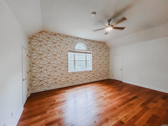 spare room with an accent wall, baseboards, vaulted ceiling, and wood finished floors