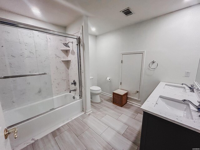 bathroom featuring double vanity, visible vents, toilet, combined bath / shower with glass door, and a sink