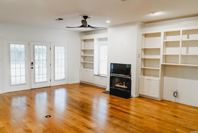 unfurnished living room featuring a fireplace with flush hearth, wood finished floors, built in features, visible vents, and crown molding