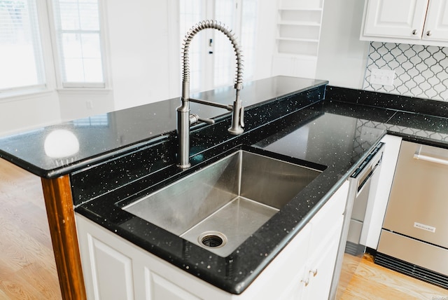 kitchen with a sink, white cabinets, stainless steel dishwasher, tasteful backsplash, and dark stone countertops