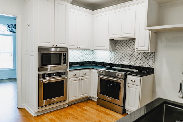 kitchen featuring stainless steel appliances, dark countertops, light wood-style flooring, and white cabinets