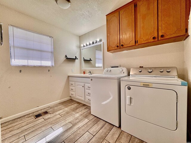 laundry area with cabinet space, light wood finished floors, visible vents, washer and clothes dryer, and a textured ceiling