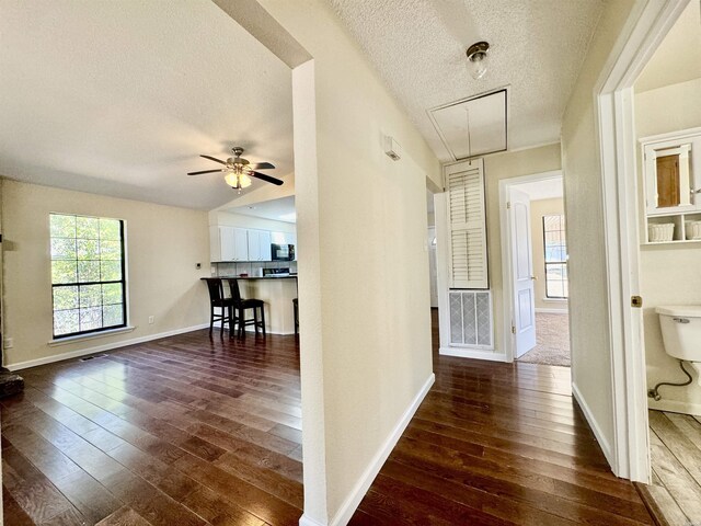 hall featuring attic access, dark wood-style flooring, a textured ceiling, and baseboards