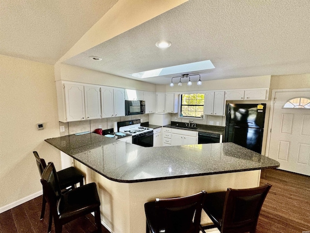 kitchen with a skylight, white cabinetry, black appliances, a peninsula, and a kitchen bar