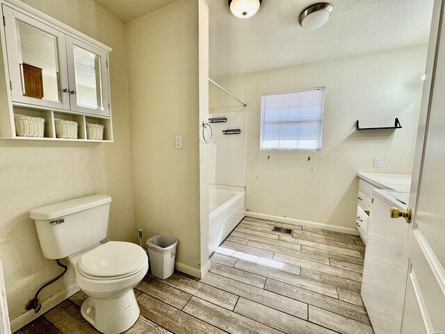 bathroom with wood finish floors, toilet, vanity,  shower combination, and baseboards