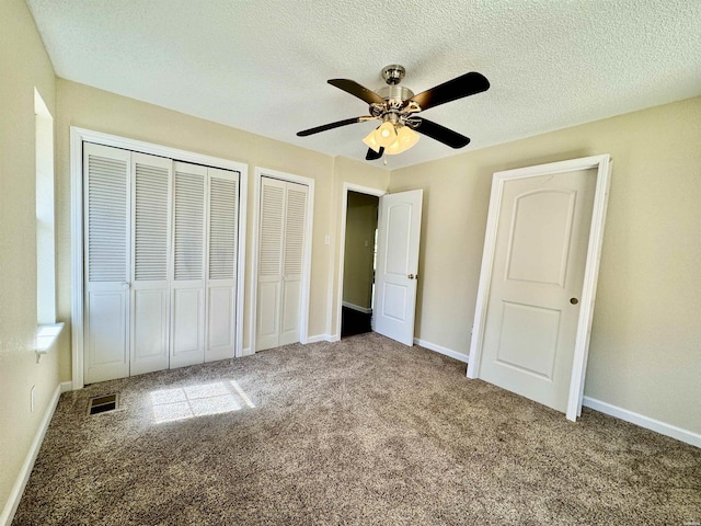 unfurnished bedroom with carpet flooring, visible vents, a textured ceiling, and two closets