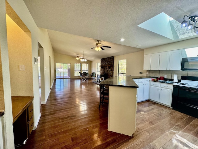 kitchen with white cabinets, a breakfast bar, a peninsula, black microwave, and gas stove