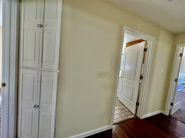 hall with dark wood-style floors, baseboards, and a textured ceiling