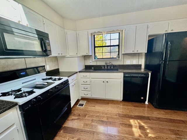 kitchen featuring dark countertops, white cabinetry, a sink, and black appliances