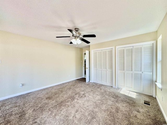 unfurnished bedroom with a textured ceiling, visible vents, baseboards, multiple closets, and carpet