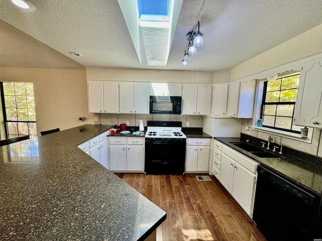 kitchen with a skylight, dark wood-style flooring, white cabinets, a sink, and black appliances