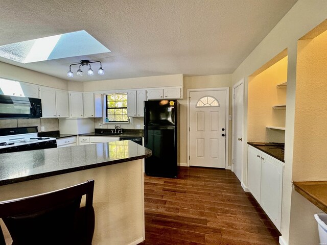 kitchen featuring a skylight, white cabinets, dark wood-style floors, black appliances, and dark countertops