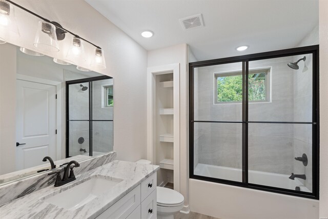 bathroom with toilet, enclosed tub / shower combo, visible vents, and vanity