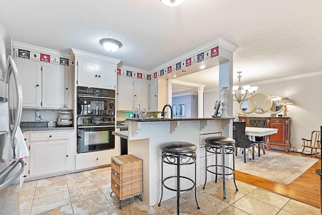 kitchen with stainless steel fridge, white cabinetry, an inviting chandelier, and dobule oven black