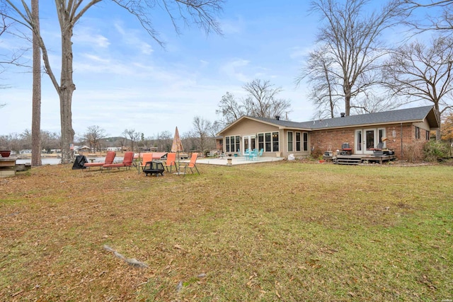 rear view of house featuring french doors, brick siding, a lawn, an outdoor fire pit, and a patio area