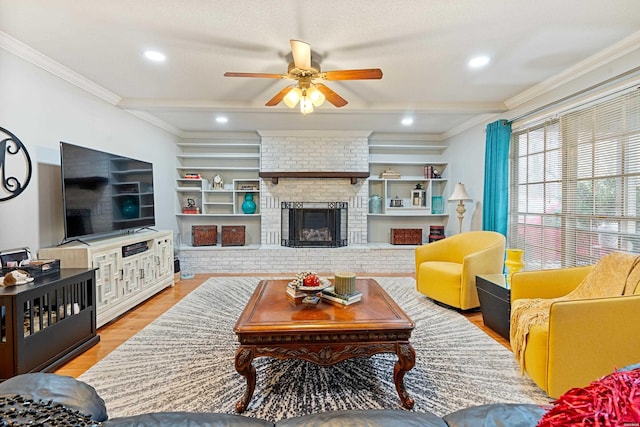 living room with built in shelves, a fireplace, crown molding, and light wood-style flooring