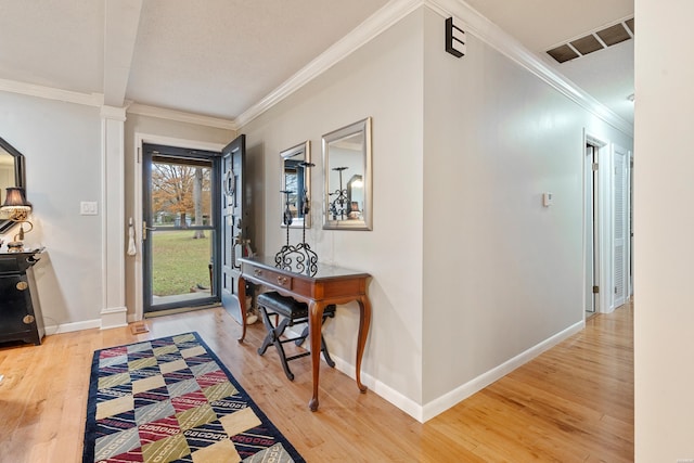 entryway with ornamental molding, visible vents, baseboards, and wood finished floors