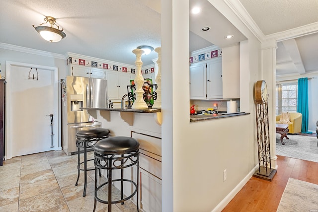 kitchen featuring white cabinets, stainless steel fridge with ice dispenser, a peninsula, crown molding, and a kitchen bar