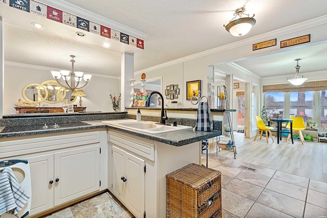 kitchen with black electric stovetop, dark countertops, hanging light fixtures, white cabinets, and a sink