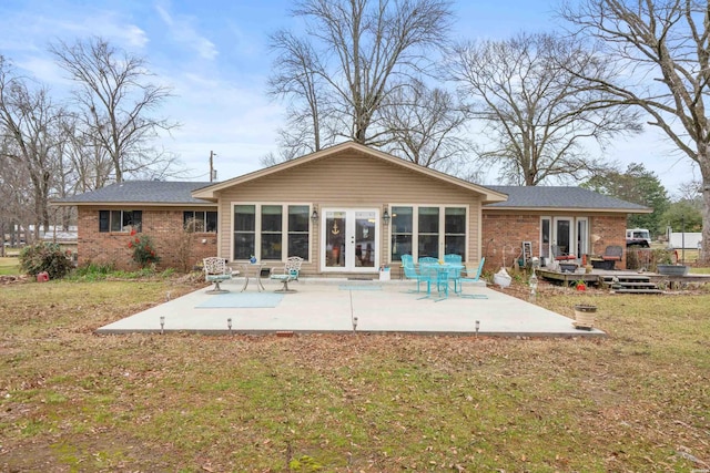 rear view of house with brick siding, a yard, a patio, and french doors