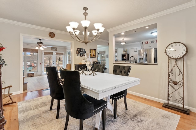 dining space with ceiling fan with notable chandelier, ornamental molding, light wood-type flooring, and baseboards