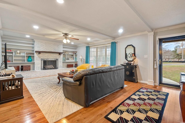 living room featuring light wood-type flooring, a fireplace, crown molding, and baseboards