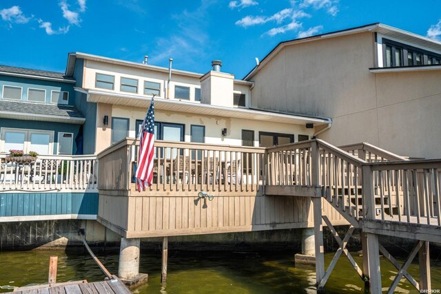 back of house with a deck with water view, a chimney, and stucco siding