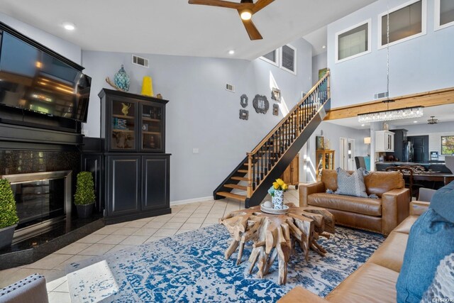 living room with light tile patterned floors, ceiling fan, a premium fireplace, visible vents, and stairs