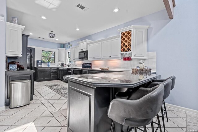 kitchen with black microwave, electric range oven, a breakfast bar, and white cabinetry