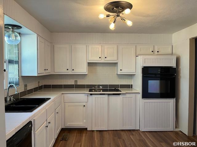 kitchen with tasteful backsplash, dark wood-type flooring, white cabinetry, a sink, and black appliances