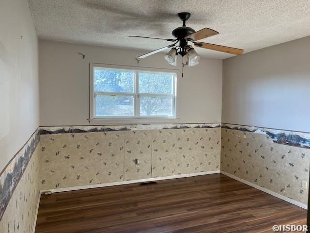 unfurnished room with a textured ceiling, wainscoting, wood finished floors, and wallpapered walls