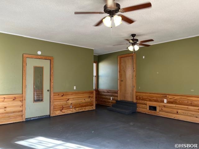 interior space with a wainscoted wall, concrete floors, a textured ceiling, and wood walls