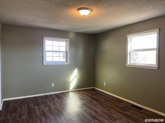 unfurnished room featuring plenty of natural light, dark wood finished floors, a textured ceiling, and baseboards