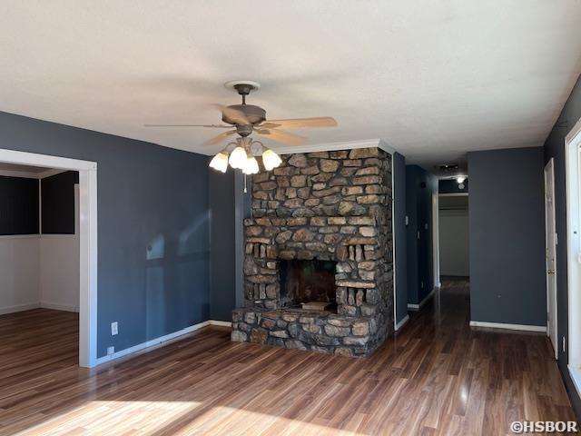 unfurnished living room with ceiling fan, baseboards, wood finished floors, and a stone fireplace