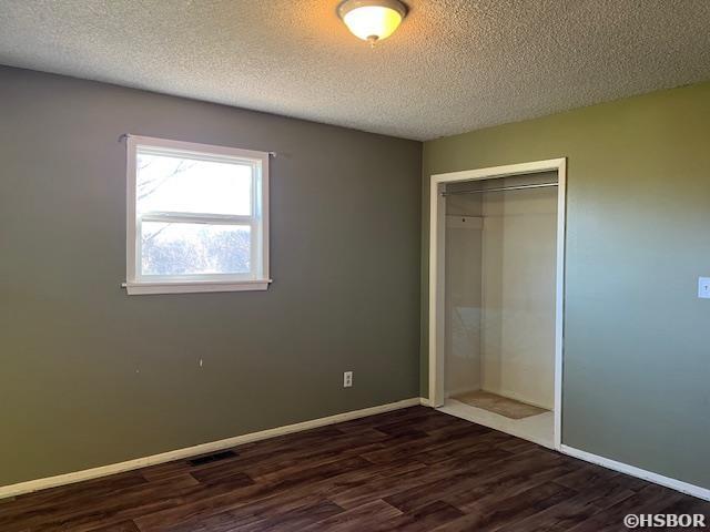 unfurnished bedroom with a textured ceiling, a closet, baseboards, and dark wood-style flooring