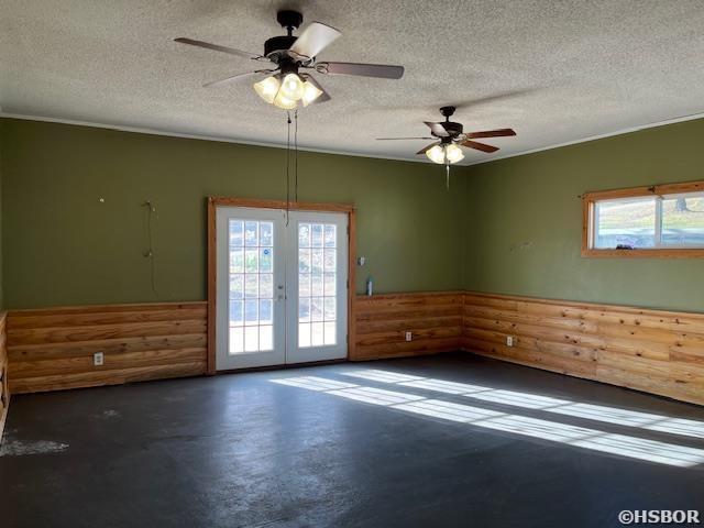 unfurnished room featuring a textured ceiling, a wainscoted wall, concrete floors, a ceiling fan, and french doors