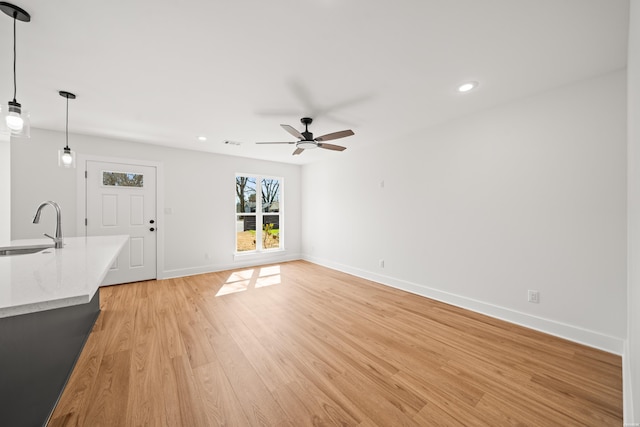 unfurnished living room featuring recessed lighting, light wood-type flooring, a sink, and baseboards