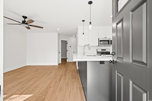 kitchen with stainless steel appliances, hanging light fixtures, light wood-style floors, a sink, and a peninsula