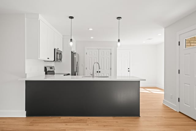 kitchen featuring stainless steel appliances, light countertops, white cabinetry, a sink, and a peninsula