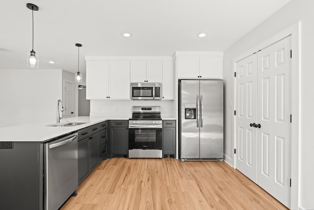 kitchen featuring stainless steel appliances, gray cabinets, light wood-style flooring, a sink, and a peninsula