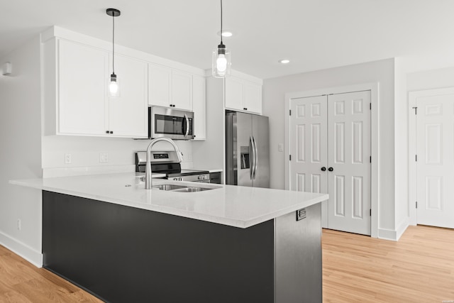 kitchen with light wood finished floors, appliances with stainless steel finishes, a peninsula, light countertops, and pendant lighting